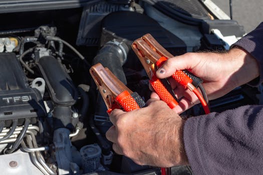 pexels-photo-5572265-5572265 Close-up of hands holding jumper cables near a car engine, ready for repair.